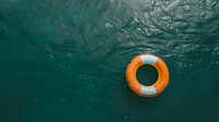 Orange and white life ring floating on turquoise ocean water surface viewed from underwater perspective with sunlight ripples and reflections creating dramatic atmosphere.