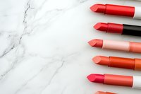 Red and coral lipsticks arranged diagonally on white marble background with copy space, flat lay composition for beauty and cosmetics marketing.