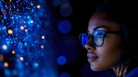 Young African American woman in glasses illuminated by glowing blue bokeh lights against dark background, side profile view creating magical atmospheric portrait.