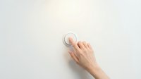 A woman's hand with light skin tone pressing a white circular button or switch on a neutral wall surface, suitable for technology, smart home, automation, and user interface concepts.