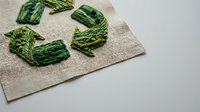 Green recycling symbol embroidered on natural burlap fabric representing eco-friendly sustainability and environmental awareness for Earth Day campaigns.