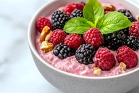 Fresh raspberries and blackberries on pink yogurt smoothie bowl garnished with mint leaves and nuts, served in gray ceramic bowl on light background.