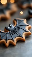 Halloween bat-shaped cookies with black icing and decorative pearls on wooden surface with warm bokeh lights creating festive autumn atmosphere.