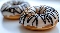 Freshly baked donuts with white glaze and dark chocolate drizzle in spider web pattern on light background, selective focus creates appetizing dessert composition.