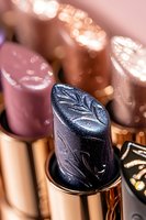 Luxurious metallic navy blue lipstick with embossed floral pattern close-up on blurred background with bokeh lights. Glamorous cosmetic product photography.