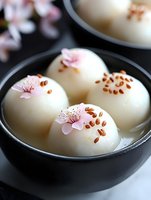 White chocolate truffles decorated with delicate pink cherry blossoms and brown seeds in black ceramic bowl, elegant Asian-inspired dessert presentation on dark background.