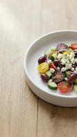 Fresh Mediterranean salad with tomatoes, cucumbers, olives, and feta cheese in white bowl on wooden table. Healthy lunch option.