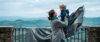 Father and son enjoying mountain view from scenic balcony overlook. Parent lifting child with blanket against panoramic landscape backdrop for family bonding moment.