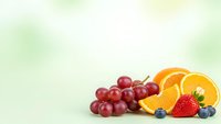 Fresh mixed fruits including red grapes, orange slices, strawberry and blueberries on light green background for healthy eating and nutrition concepts.
