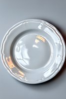 Empty white ceramic plate with ornate scalloped edges and glossy finish on neutral gray background, isolated view from above for culinary and dining presentations.
