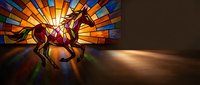 Stained glass window depicting horse and rider silhouette with vibrant colored panels casting rainbow light shadows on wooden floor in church or cathedral interior.