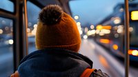 Person in orange knit hat with pom-pom looking out bus window at evening city lights and traffic during urban commute journey.