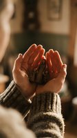 Cupped hands holding coffee beans in warm sunlight, cozy knit sweater sleeves visible, rustic kitchen background with golden hour lighting for coffee concepts.