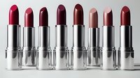 Row of eight luxury lipsticks in silver tubes displaying rich berry, nude and red shades arranged on white background for cosmetic advertising.