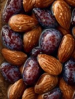 Fresh ripe purple plums and raw almonds mixed together in macro shot, showing natural texture and details of nuts and fruits for healthy eating concept.