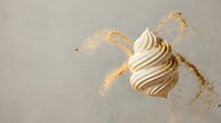 Elegant white chocolate swirl with golden cocoa powder splash on neutral background for luxury dessert and confectionery marketing materials.