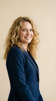Confident middle-aged Caucasian businesswoman with curly blonde hair smiling in navy blue suit jacket against neutral beige background for corporate headshots.