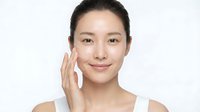 Young Asian woman applying facial cream with gentle touch, skincare routine, beauty treatment, moisturizing face, natural makeup, wellness lifestyle, spa concept.