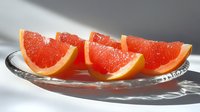 Fresh juicy grapefruit wedges on glass plate with dramatic shadows. Bright red citrus segments arranged in row showing pulp texture and natural light.