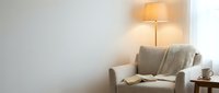 Cozy modern living room corner with beige armchair, warm floor lamp lighting, and minimalist decor creating peaceful home interior atmosphere.