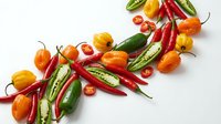 Colorful assortment of fresh hot chili peppers including red cayenne, green jalapeno and orange habanero varieties isolated on white background for cooking.
