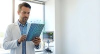 Professional male doctor examining medical X-ray scan in modern hospital office. Healthcare specialist analyzing patient radiography results for diagnosis.