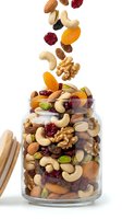 Mixed nuts and dried fruits falling into glass jar on white background, isolated for packaging and food design use.