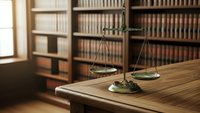 Vintage brass scales of justice on wooden desk in traditional law library with leather-bound books for legal consultation and attorney services.