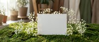 Blank white card surrounded by delicate baby's breath flowers on moss surface with soft natural lighting for wedding invitations and greeting cards.