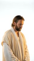 Bearded man in traditional white robes looking down thoughtfully, spiritual leader or biblical character portrait on white background for religious content.