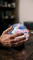 Elderly hands holding glowing crystal ball with colorful lights for fortune telling and mystical predictions in cozy home setting.