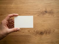 Hand holding blank white business card against wooden surface for branding and corporate identity mockup presentations.
