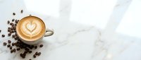 Cappuccino with latte art heart design on marble surface surrounded by scattered coffee beans, overhead view for café, restaurant, and beverage marketing.