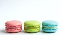 Three colorful French macarons in pink, green and blue arranged in row on white background. Sweet dessert cookies for bakery menu design.