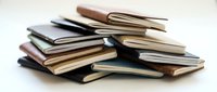 Stack of various leather notebooks and journals piled together on white background, showcasing different colors and sizes for stationery concepts.