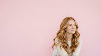 Young woman with long wavy auburn hair wearing white shirt against pink background, suitable for beauty, lifestyle, and portrait design projects.