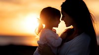Silhouette of loving mother and daughter sharing tender moment at sunset, backlit with golden sun creating atmospheric glow and emotional connection between parent and child.