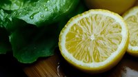 Fresh lemon slices with water droplets and green mint leaves on wooden cutting board for healthy cooking and natural beverages preparation.