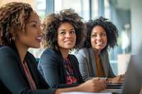 Young African American businesswomen with natural curly hair smiling during corporate meeting in modern office space, showing diversity and teamwork.
