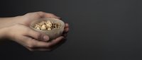 Hands holding wooden bowl filled with golden bitcoins on dark background representing cryptocurrency investment and digital wealth concept.