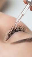 Professional eyelash extension application with glass dropper applying serum to enhance natural lashes in modern beauty salon treatment.