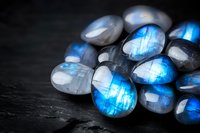 Luminescent moonstone and labradorite gems with bright blue flashes and iridescent sheen on dark textured background, macro mineral photography.