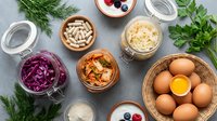 Probiotic foods and supplements flat lay with fermented vegetables, kimchi, eggs, and capsules on gray background for healthy gut concept.