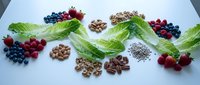 Fresh organic superfood ingredients arranged on white background with leafy greens, mixed berries, nuts and seeds for healthy nutrition and wellness.