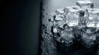Transparent ice cubes stacked on wet dark surface with water droplets and reflections, suitable for beverage, drink, and cooling concept designs.