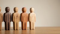 Wooden figures in various natural tones standing in a row on wooden surface, representing diversity, teamwork, community, and human connection for business and organizational concepts.