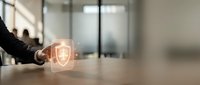 Businessman touching glowing digital shield icon on desk in modern office, symbolizing cybersecurity, data protection, and network safety.