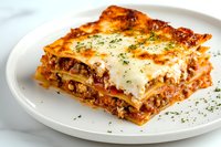 Classic layered lasagna with ground beef, melted mozzarella and parmesan cheese, rich tomato sauce, and fresh herbs served on white plate, close up view of single portion.