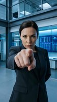 Confident businesswoman pointing finger at camera in modern corporate office with glass architecture and digital displays for leadership concepts.