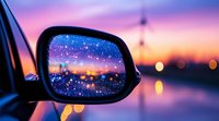 Starry night sky reflected in car side mirror against vibrant sunset backdrop with glowing city lights and bokeh effect creating magical evening atmosphere.
